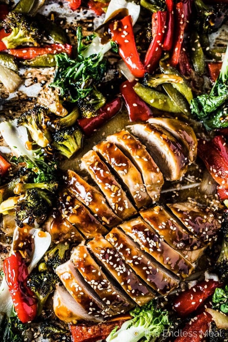 Sliced chicken bread cooked on a sheet pan with veggies and sauce.