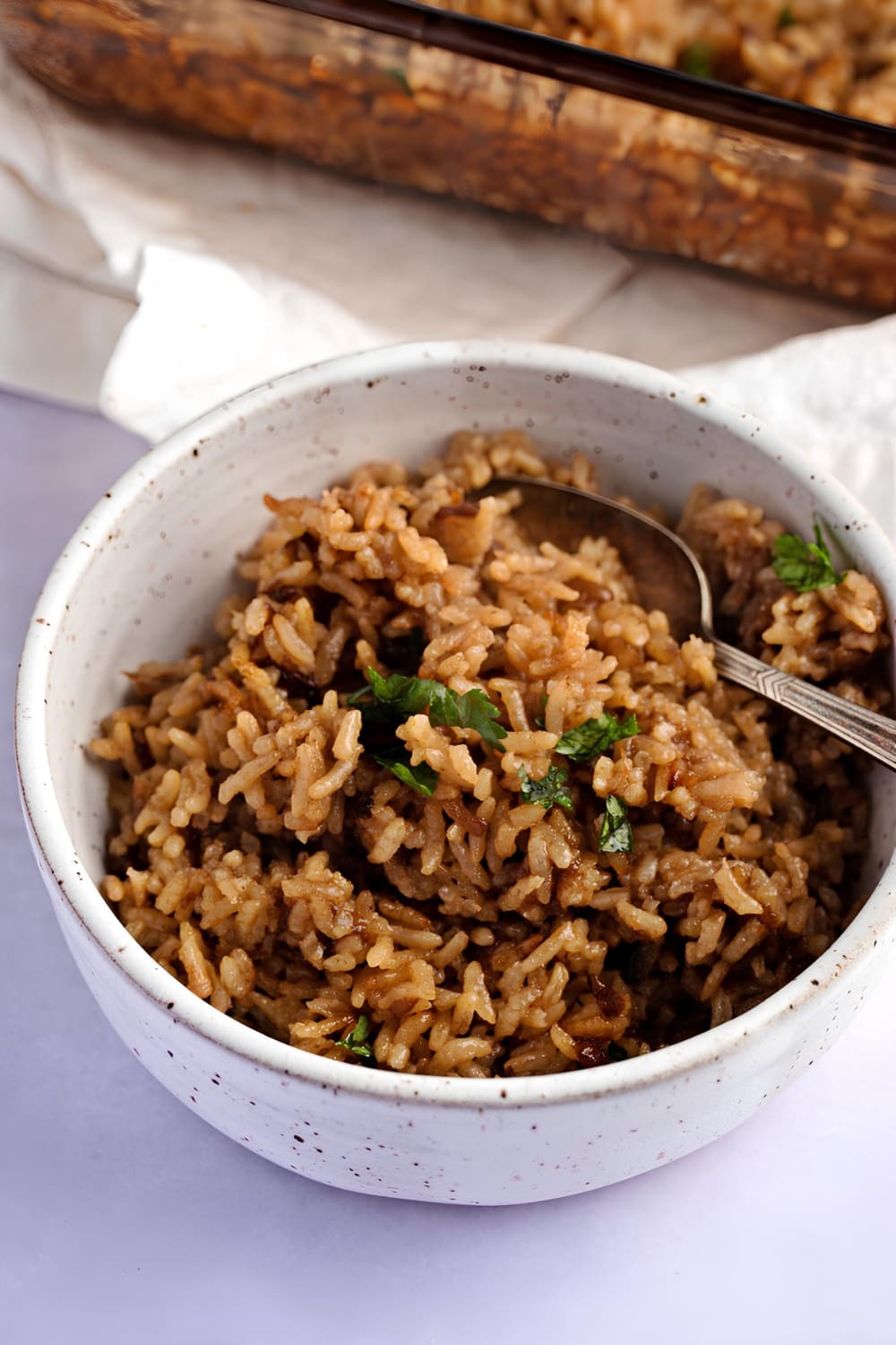 Brown colored rice in a white bowl with spoon.