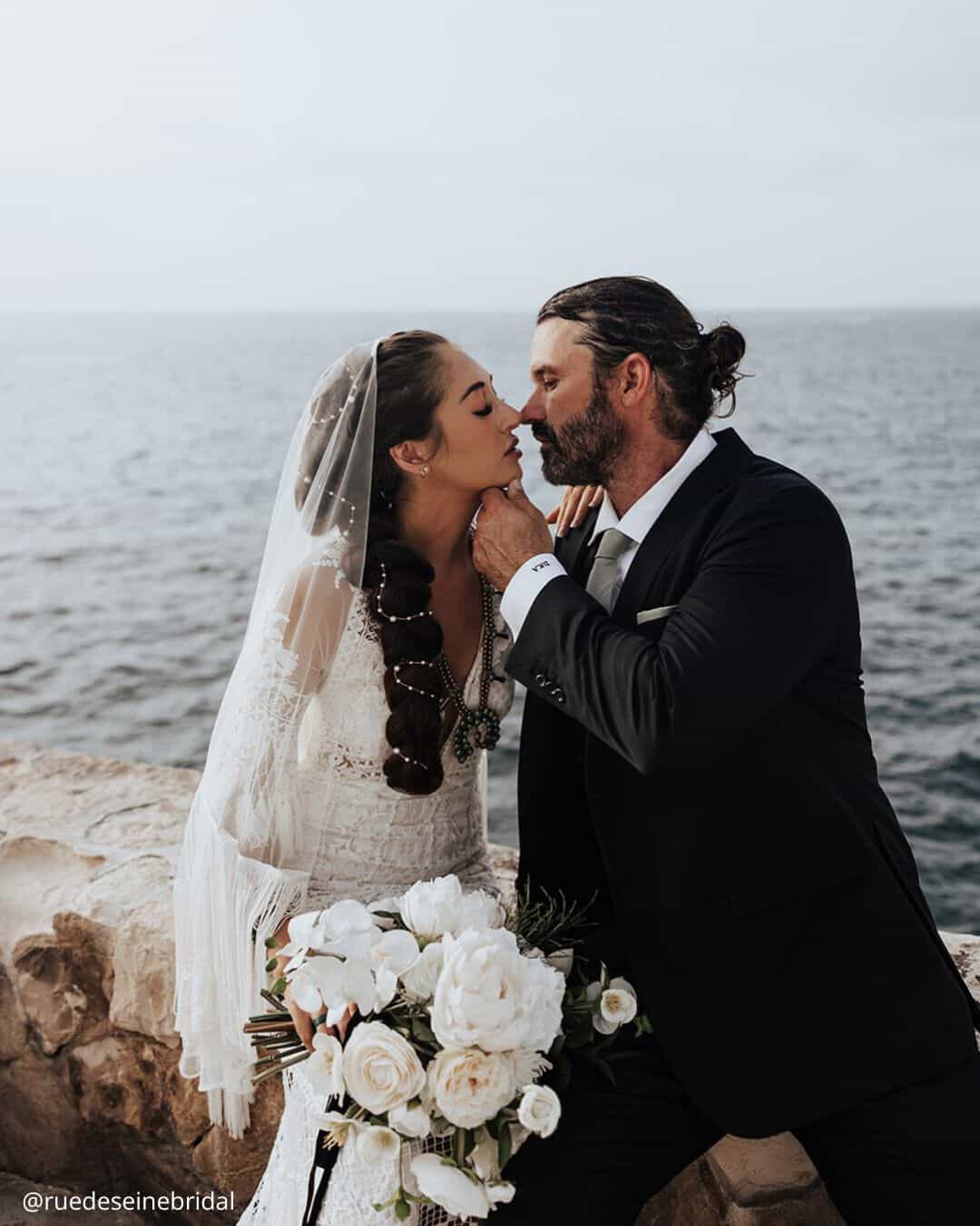 wedding photos happy brides kissing in her bouquet in hands on the sea background ruedeseinebridal